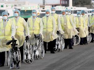 Ministry of Health workers, dressed in protective suits, wait on the runway at Kuwait International Airport to greet Kuwaitis returning from Frankfurt on 26 March 2020