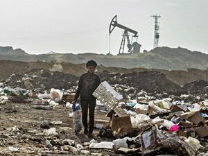 A Syrian child sifts through a garbage dump near an oil field in the countryside of Malikiya in northeast Syria, on January 12, 2021. On the dry plains outside the city of Al-Malikiyah, a dozen people wrapped up against the cold rip open the black plastic bags, in a desperate search for something to sell, repurpose or even eat. Across the road, an oil pump swings back and forth in this resource-rich region controlled by US-backed Kurdish forces.  Delil SOULEIMAN / AFP