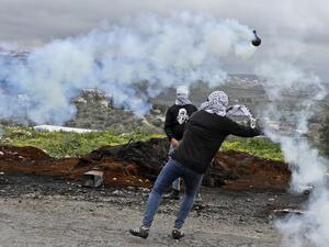 Palestinian protesters use slingshots to hurl rocks amid billowing tear gas during clashes with Israeli troops in the village of Kfar Qaddum near the Jewish settlement of Qadumim (Kedumim) in the occupied West Bank, following a demonstration against the expropriation of land by Israel, on January 15, 2021. JAAFAR ASHTIYEH / AFP