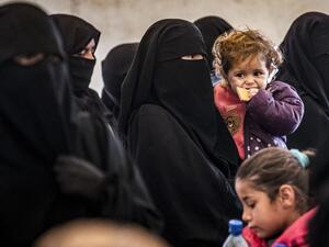 A veiled woman stands carrying a child alongside others during the release of persons suspected of being related to Islamic State (IS) group fighters from the Kurdish-run al-Hol camp in Hasakeh governorate in northeastern Syria, on January 19, 2021. Delil SOULEIMAN / AFP