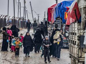 A man carries a child as he walks with other women and children ahead of a member of the Syrian Kurdish internal security services known as Asayish as they head towards trucks, during the release of persons suspected of being related to Islamic State (IS) group fighters from the Kurdish-run al-Hol camp in Hasakeh governorate in northeastern Syria, on January 19, 2021. Delil SOULEIMAN / AFP