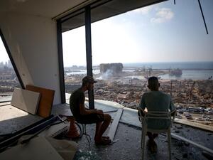In this file photo taken on August 6, 2020, two men gaze at the devastated Beirut port from a damaged building in the nearby neighbourhood of Mar Mikaehl, two days after a massive blast there shook the Lebanese capital. Six months after a massive explosion ripped through Beirut, donors say that most of the emergency aid they pledged for Lebanon's needy has been disbursed. But some non-governmental organisations say they have hardly received anything, or seen funds they have received lose their value as they