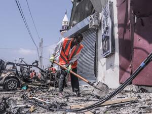 A rescue worker clears debris with a shovel at the site of a suicide car bombing attack near a security checkpoint in Mogadishu on February 13, 2021. Three people were killed and eight wounded after a car bomb detonated near a security checkpoint in the Somali capital Mogadishu, a security official and witnesses said. Abdirazak Hussein FARAH / AFP