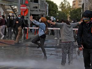 Cypriot protesters react as police fire water cannon to disperse them during a demonstration against government corruption and coronavirus restrictions, in the capital Nicosia on February 13, 2021. Cypriot police used water cannon and tear gas to break up a rare protest in the capital, as hundreds demonstrated against government corruption and coronavirus restrictions. Christina ASSI / AFP