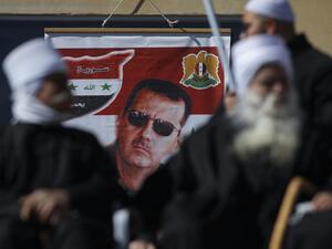 Members of the Druze community sit near a billboard bearing the portrait of Syrian President Bashar Assad during a rally in the village of Majdal Shams in the Israeli-annexed Golan Heights on February 14, 2021, to protest the 1981 Israeli annexation law of the strategic plateau which the Jewish state captured from Syria during the 1967 Arab-Israeli war. JALAA MAREY / AFP