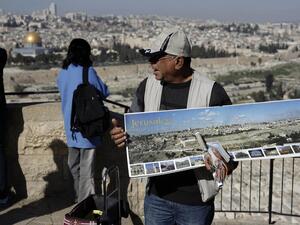 A vendor sells souvenir postcards to tourists watching Jerusalem's Old City from the panoramic view of the Mount of Olives, January 2019 (AFP)