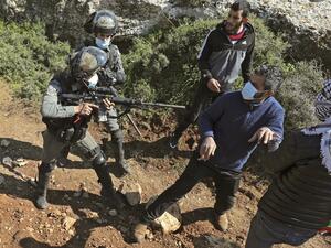 An Israeli soldier points his gun towards a Palestinian