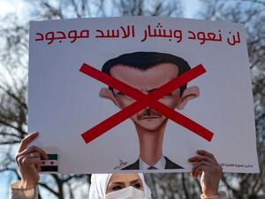 A Syrian woman holds up a banner that reads, 'We will not return as long as (Syrian President) Assad is present'
