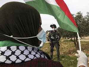 A Palestinian woman waves the national flag at an Israeli border guard 