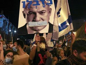 Israeli protesters hold a poster of PM Netanyahu gagged by a surgical protection mask 