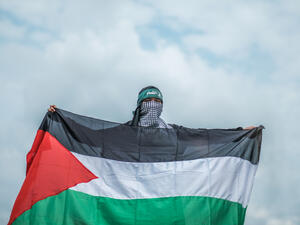 A young teenage Muslim girl wearing abaya and hijab holding a Palestine flag and a head gear with Arabic language means "Brigade AlQassam" which related to an army under Hamas