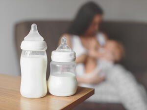 Bottles with breast milk on the background of mother holding in her hands and breastfeeding baby