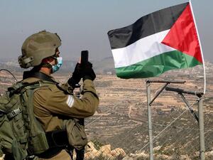 Israeli soldier facing a Palestinian flag