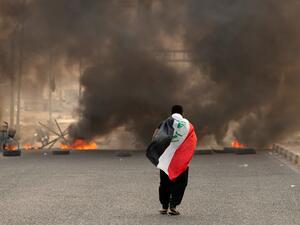 A supporter of Iraqi Shiite cleric Moqtada Sadr carries the Iraqi flag as he walks down a road blocked by burning tyres during a demonstration in Iraq's southern city of Basra on August 29, 2022. (Photo by Hussein Faleh / AFP) Green Zone