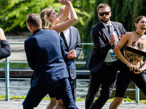 Topless demonstrators with the slogan on their skin reading "GAS EMBARGO NOW" protest as the security personnel tries to take them away from the German Chancellor Olaf Scholz during the Federal Government's Open Day event at the Chancellery in Berlin on August 22, 2022. (Photo by JENS SCHLUETER / AFP) Topless women