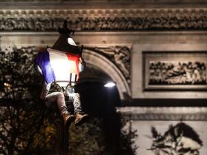 A football fan, sitting on a lamp post next to the Arc de Triomphe, celebrates after France's victory over Morocco in the Qatar 2022 World Cup semi-final, on the Champs-Elysees in Paris on December 14, 2022. (Photo by Thibaud MORITZ / AFP)