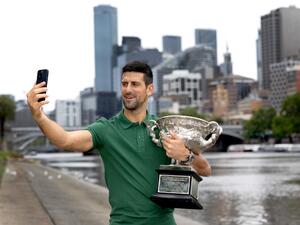 This handout picture released by Tennis Australia on January 30, 2023, shows Serbia's Novak Djokovic takes a selfie with the Norman Brooks Challenge Cup next to the boat sheds on the Yarra River, the same spot of his first Australian Open trophy celebrations, in Melbourne. (Photo by FIONA HAMILTON / TENNIS AUSTRALIA / AFP)
