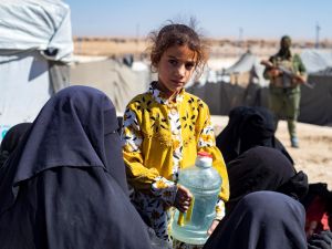 A girl looks on while holding a water container as members of the Syrian Kurdish Asayish security forces inspect tents at the Kurdish-run al-Hol camp. (Photo by Delil SOULEIMAN / AFP) ISIS members