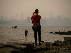 A man stands before the New York City skyline and east river shrouded in smoke, in Brooklyn on June 6, 2023. (Photo by Ed JONES / AFP) New York city