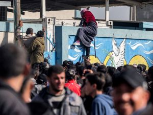 سيدة تتسلق جدران أحد مستودعات "الأونروا"  بعد انتظارها في طابور الحصول على حصص الطحين، في رفح جنوب غزة