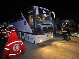 Members of the Syrian Red Crescent and Civil Defence stand by as a convoy of buses carrying rebel fighters and civilians from the Eastern Ghouta enclave town of Harasta arrives in the town of Qalaat al-Madiq, about 45 kilometres northwest of the central city of Hama, early on Mar. 23, 2018. 
(OMAR HAJ KADOUR / AFP)