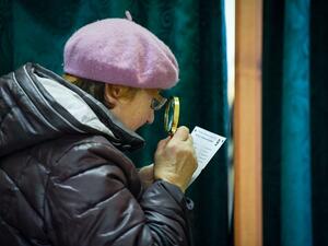 An elderly woman uses a magnifying glass to read her ballot papers as she prepares to cast her ballot at a polling station in Ogre, Latvia, during general elections on October 6, 2018. 
Ilmars ZNOTINS / afp