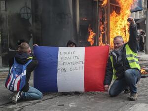 Yellow Vest protesters hold a French national flag reading "Freedom, Equality, Fraternity, my Ass !" as they pose in front of a newsstand set alight during clashes by protesters on the Champs-Elysees in Paris on March 16, 2019. (AFP/ File)