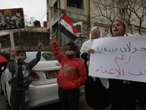 Residents of the Golan Heights raise Syrian flags and a banner with portraits of the Syrian President Bashar al-Assad during a protest against the backing of Israel's capture of the Golan Heights by the US president. (AFP)