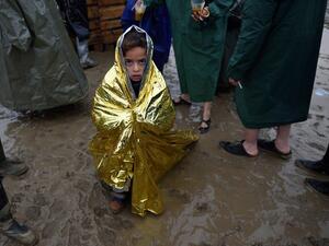 A child wrapped in a survival blanket looks as migrants queue for hot soup on March 13, 2016, in a makeshift camp at the Greek-Macedonian border, near the Greek village of Idomeni, where thousands of refugees and migrants are stranded by the Balkan border blockade. (AFP/Daniel Mihailescu)
