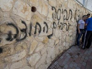 Arab Israeli men stand next to graffiti reading in Hebrew "Arabs Out" on the wall of a mosque in the northern Israeli city of Umm al-Faham on April 18, 2014 (JACK GUEZ / AFP)