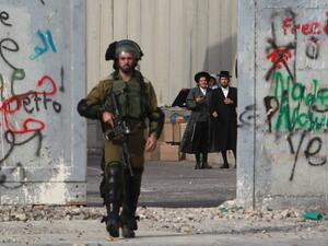 Orthodox Jewish men stand behind Israel's controversial separation barrier as a soldier makes his way through the West Bank entrance to Bethlehem, October 12, 2015. (AFP/File)