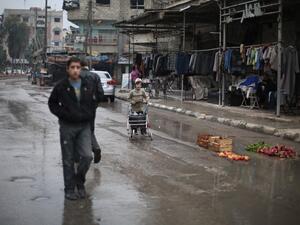 Syrians walk in the rain past a shop in the town of Kfar Batna, on the outskirts of the capital Damascus, November 17, 2015. (AFP/File)