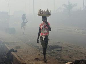 Vendors cover their nose as they walk through smoke emanating from the Olusosun dump site in Lagos, Nigeria (AFP/File Photo)