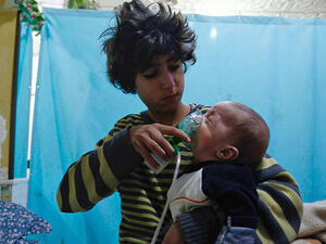 A Syrian child holds a gasmask to an infant's face in a makeshift hospital in Eastern Ghouta following a gas attack (AFP/FILE)