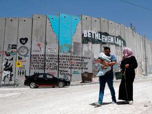 A Palestinian family walk past new graffiti painted on Israel's controversial separation barrier (AFP/File Photo)
