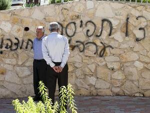 Arab Israeli men stand next to graffiti reading in Hebrew "Arabs Out" on the wall of a mosque in the northern Israeli city of Umm al-Faham. AFP Photo

