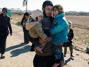 An Iraqi man carries his children near the town of Bartella as people return to their liberated neighbourhoods in eastern Mosul on January 7, 2017, (AFP)