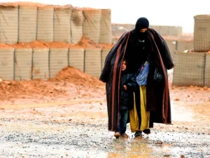 A Syrian refugee from the informal Rukban camp, which lies in no-man's land off the border between Syria and Jordan, walks in the rain on March 1, 2017. She is sheltering a young child outside a U.N.-operated medical clinic immediately on the Jordanian side (AFP/File)