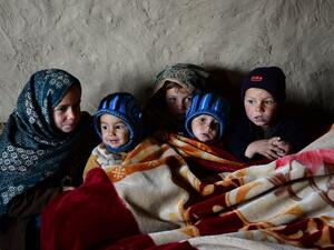 In this photograph taken on January 18, 2017, Afghan children warm themselves with a blanket inside a mud house at a refugee camp on the outskirts of Laghman.  (AFP/Noorullah Shirzada)