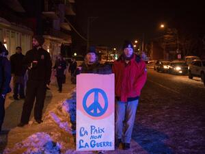 People stand with a peaceful sign near the Québec City Islamic cultural center after a shooting occurred in the mosque on Sainte-Foy Street in Quebec city on January 29, 2017. (AFP/Alice Chiche)