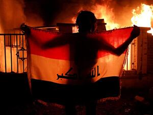 Man holding a national flag while demonstrators burn municipal complex (Twitter)