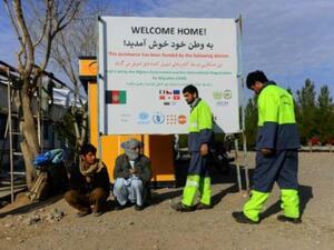 صورة تظهر المهاجرين الأفغان العائدين من إيران لدى جلوسهم تحت لافتة لمنظمة الهجرة الدولية في هرات

