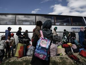 Refugees stand near a bus as they wait to be transferred to a hospitality center during a police operation at a refugee camp at the border between Greece and Macedonia, near the village of Idomeni on May 25, 2016. (AFP/Yannis Kolesidis)