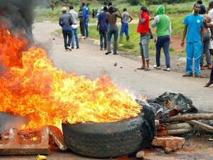 ظاهرون يقفون خلف حاجز مشتعل خلال تظاهرة على طريق مؤدية إلى العاصمة هاراري
