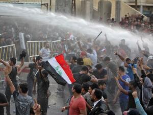 Iraqi protesters chanting slogans and waving national flags are sprayed with water cannon by security forces in clashes in protests against unemployment and lack of basic services Baghdad's Tahrir Square on July 20, 2018. (AFP/Ahmad Al-Rubaye)
