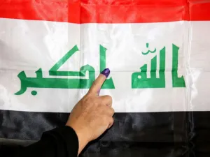 An Iraqi woman shows her ink-stained index finger before a national flag after having cast her vote in the country’s parliamentary election, in the capital Baghdad's Karrada district on May 12. (AFP)