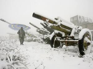 A Lebanese man holding a umbrella walks past abandoned Israeli cannons during a snow storm in the southern village of Khiam, on the Israeli-Lebanese border. [AFP]