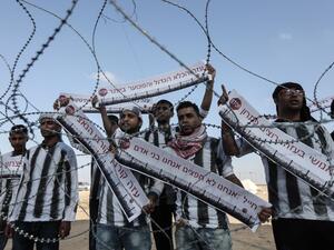 Palestinian demonstrators dressed in striped t-shirts marking internment camp outfits hold up signs with slogans written in Hebrew/AFP