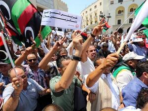 Libyan protesters shout slogans waving national flags during a demonstration on the Algeria Square to demand the removal of arms and the evacuation of unofficial armed groups and the implementation of the General National Congress (GNC)'s decision on July 7 (AFP)