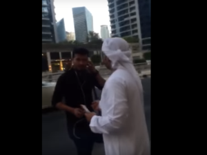 Screenshot from the video showing two men in Emirati traditional attire while handing random people in the street cash money.